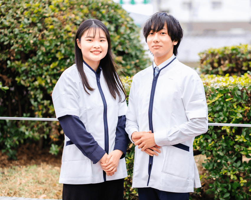 白衣風のユニフォームを着た男女2人が屋外で並んで微笑んでいる